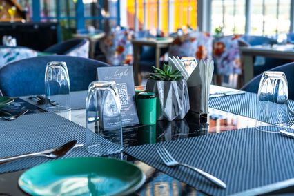 Architectural photograph of a restaurant interior with tables, chairs, and glasses. Beautiful dining room setting with natural light.