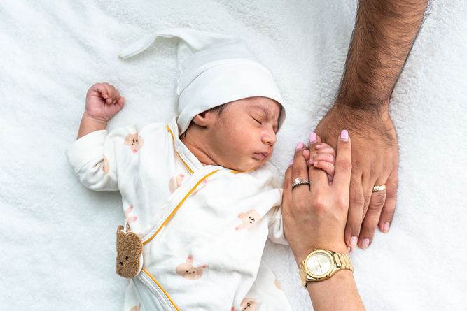 Newborn baby sleeping gently with parents family holding hands lovingly.