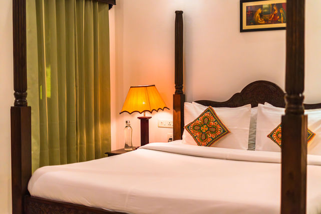 Architectural photograph of a cozy bedroom with a four-poster bed, lamp, and decorative pillows. HOSPITALITY.