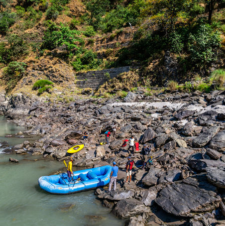 People prepare raft for river rafting adventure near large rocks and mountains.