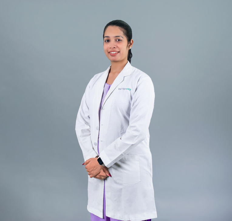 Smiling doctor in white coat stands, with text visible on the coat.