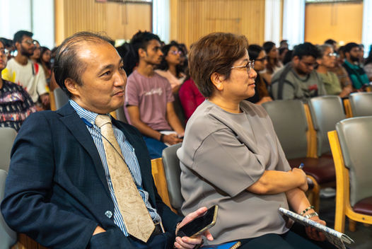 Attendees in a conference listening attentively, with visible text and background context.