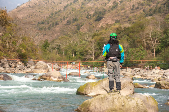 Person standing on a rock looking at the river near the mountains.