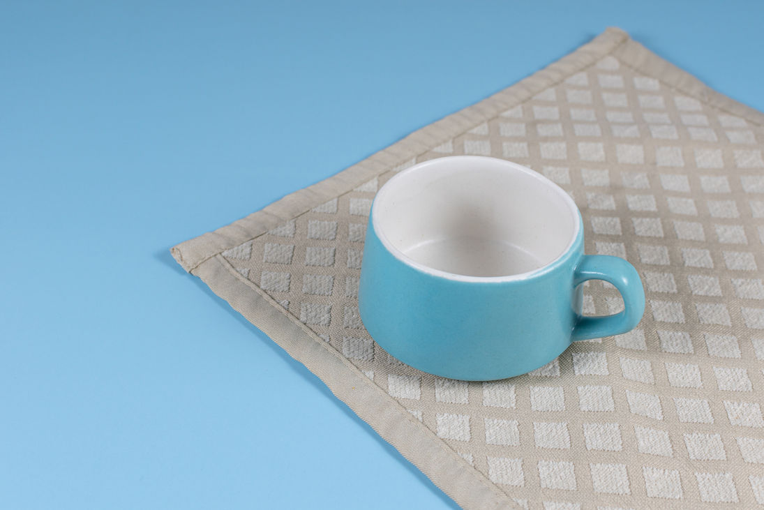 Blue mug sits on a beige textured placemat against a blue background.