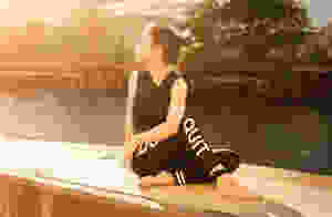 woman wearing black fitness outfit performs yoga near body of water