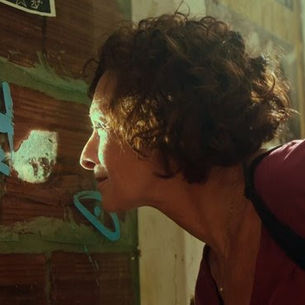 Fotograma do filme Lispectorante de Renata Pinheiro. Marcélia Cartaxo olha na greta de uma parede.