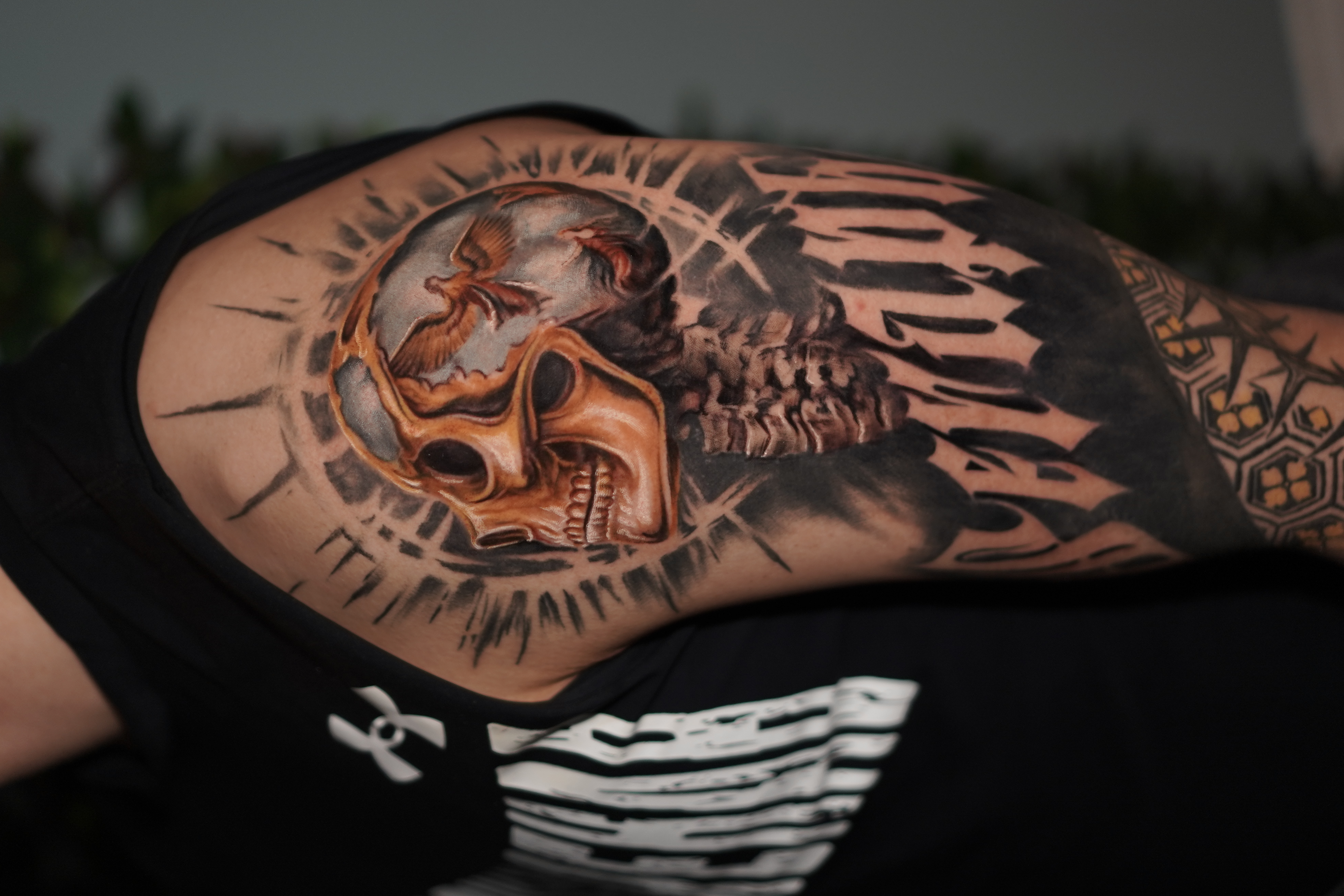 Upper-arm tattoo of a realistic skull with a dove inside a rayed halo above lettering