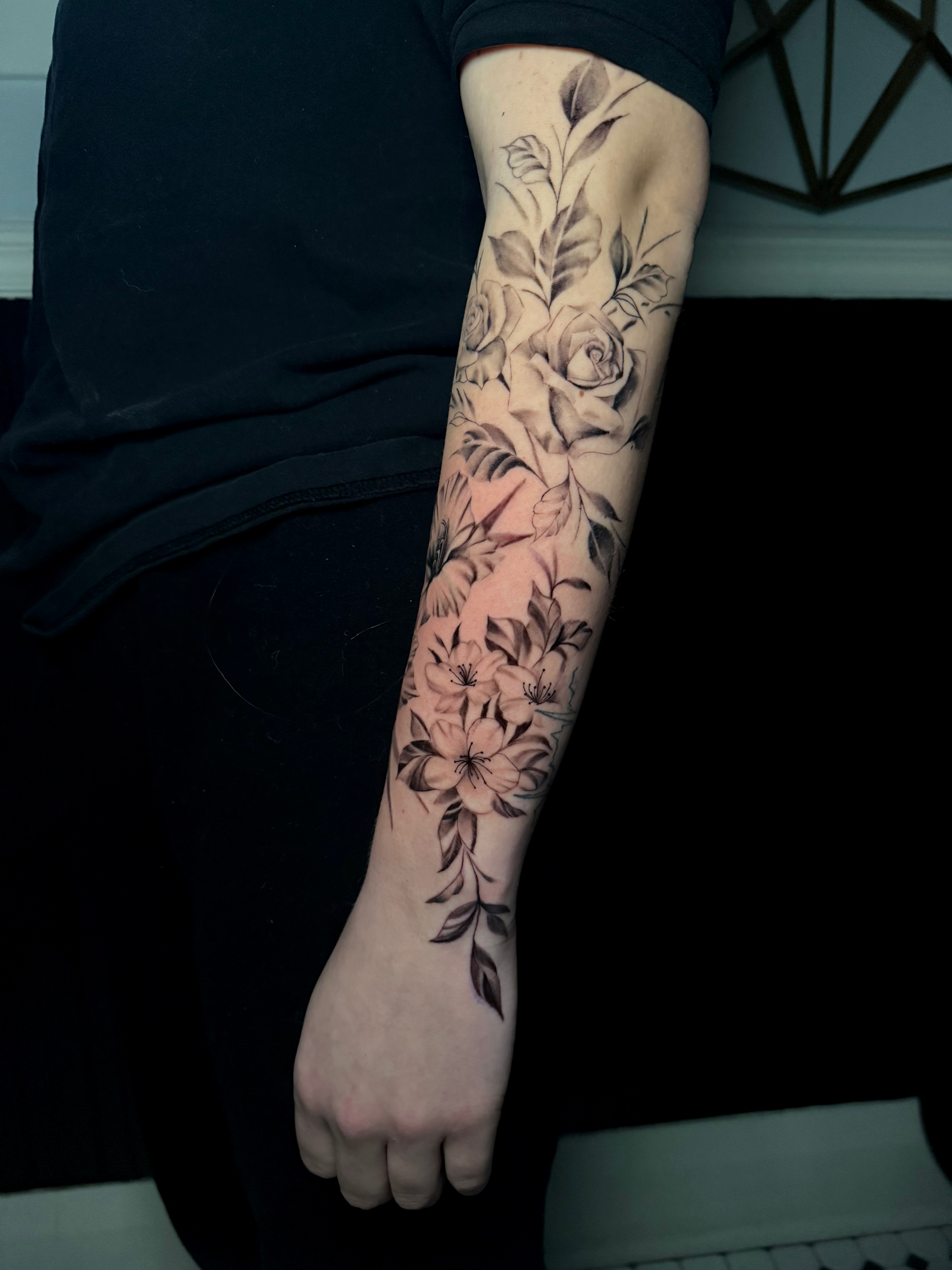 Black-and-grey floral forearm sleeve of roses, lilies and foliage