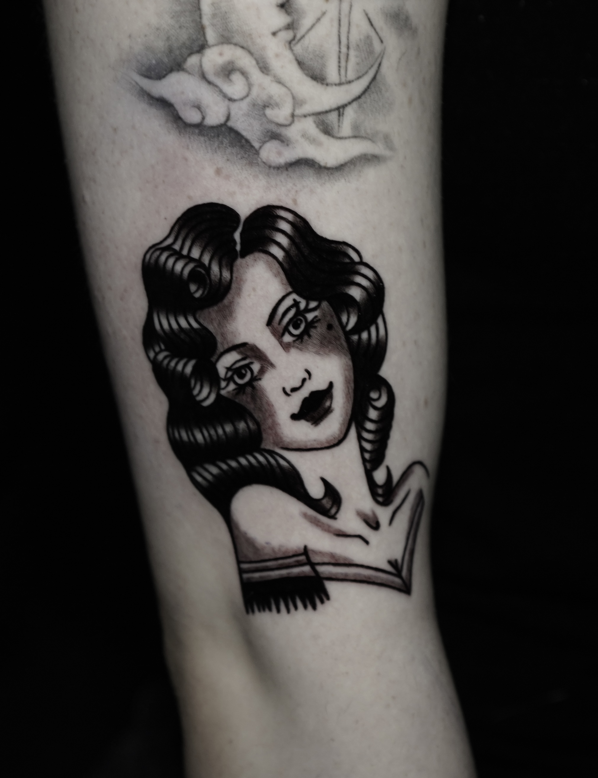 Lower-leg blackwork tattoo of a traditional woman's head with a cloud above it