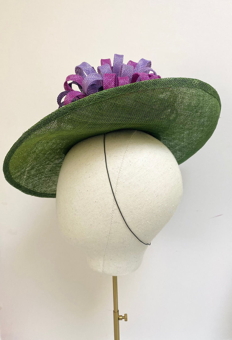 Thumbnail: A large brimmed green hat with purple decoration is displayed on a mannequin head