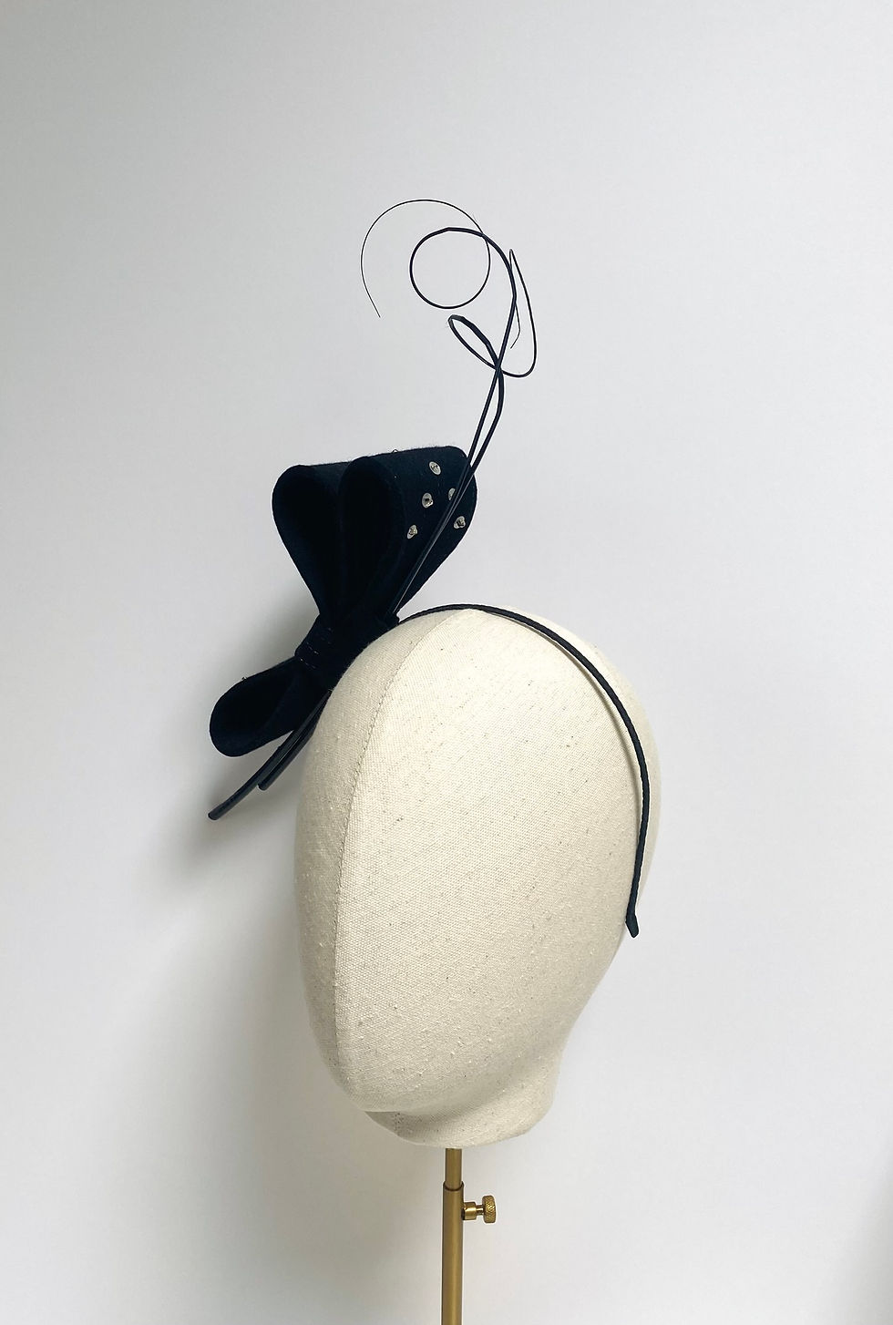 Thumbnail: A large black felt bow headband decorated with ostrich quill feathers and silver sequins is displayed on a mannequin head