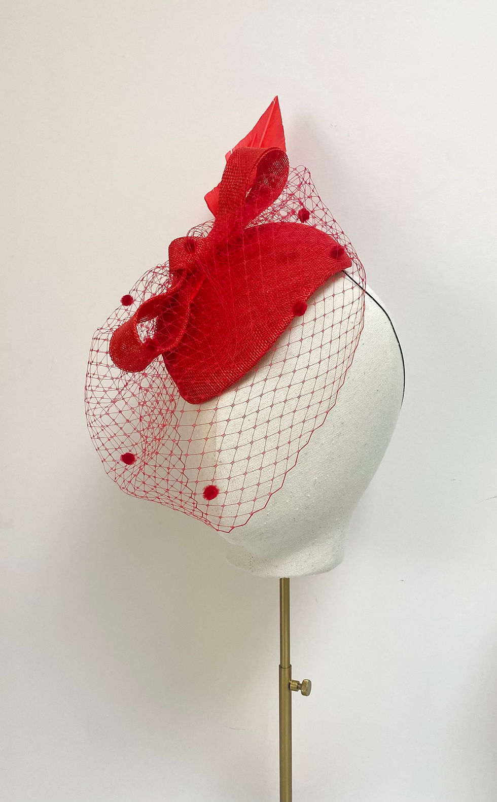 Thumbnail: A bright red sinamay wedding hat with veil is displayed on a mannequin head
