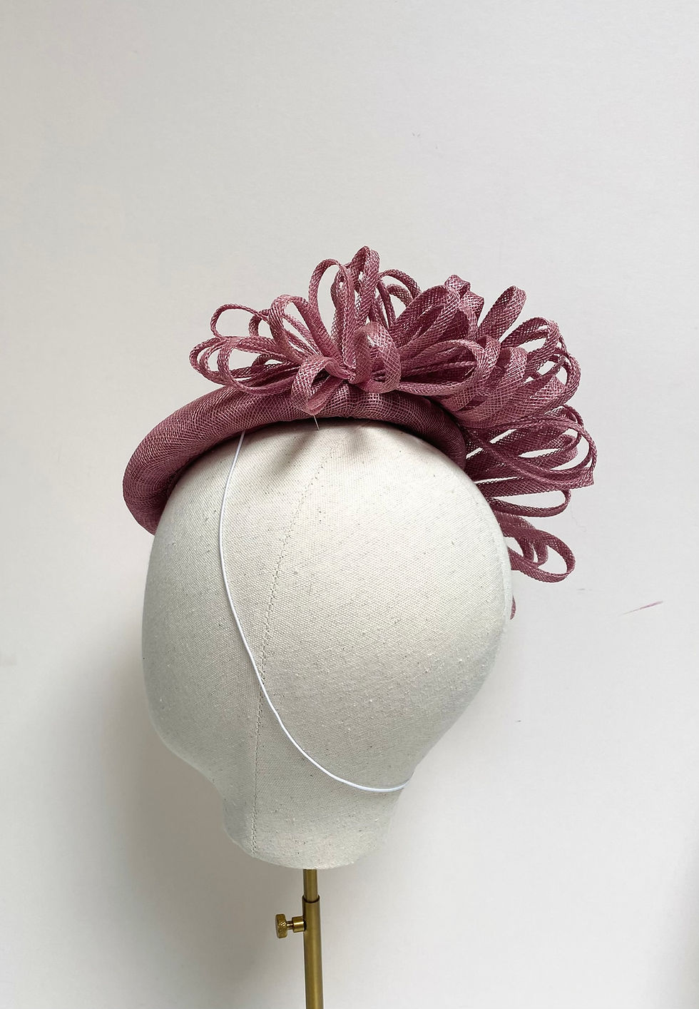 Thumbnail: A dusky pink sinamay hat decorated with matching loops is displayed on a mannequin head