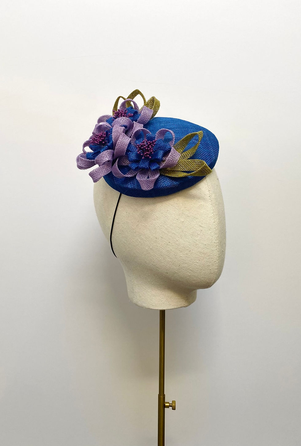 Bright blue wedding hat with looped flowers and leaves displayed on a mannequin head