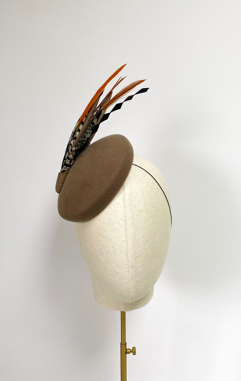 Thumbnail: A light brown felt round wedding guest hat with feathers is displayed on a mannequin head
