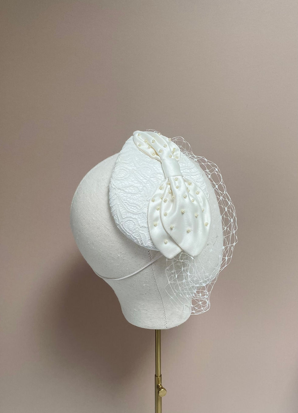 Thumbnail: An ivory lace wedding headpiece with a veil is displayed on a mannequin head