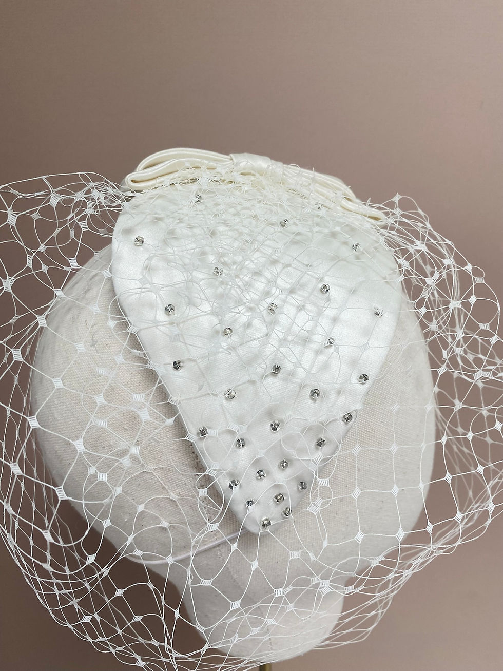Thumbnail: An ivory vintage style bridal beaded headpiece with bow and veil is displayed on a mannequin head