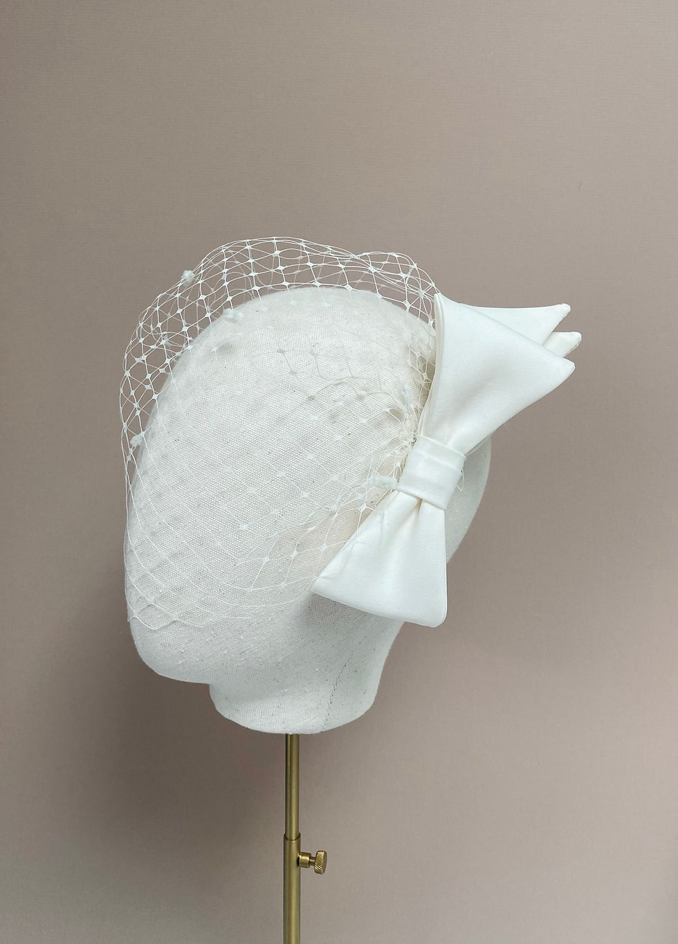 Thumbnail: An ivory bridal birdcage veil with spot netting and a bow at the side is displayed on a mannequin head