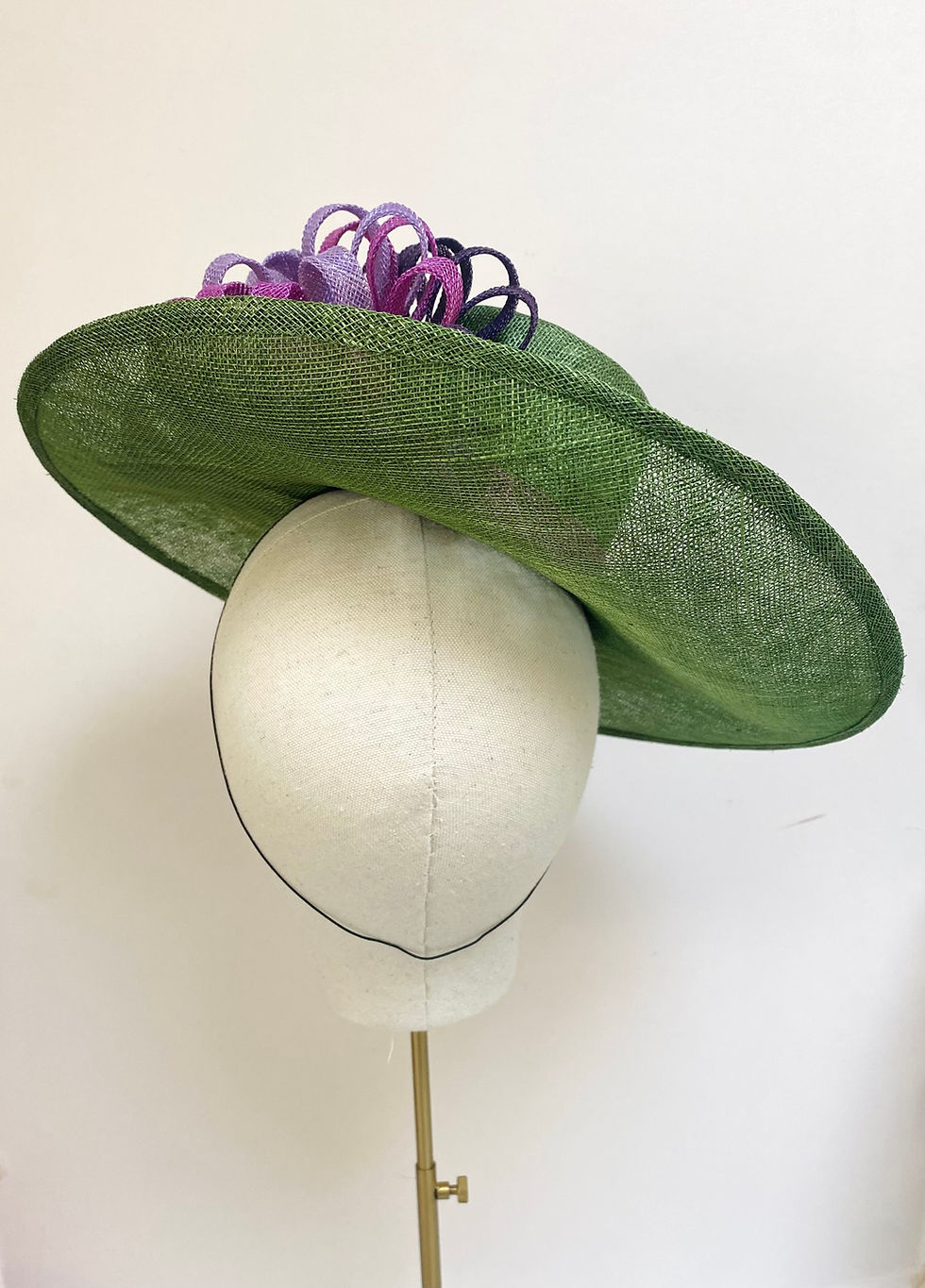 Thumbnail: A large brimmed green hat with purple decoration is displayed on a mannequin head
