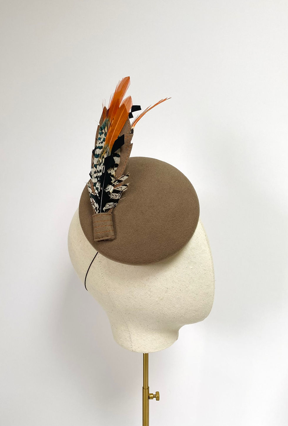 Thumbnail: A light brown felt round wedding guest hat with feathers is displayed on a mannequin head