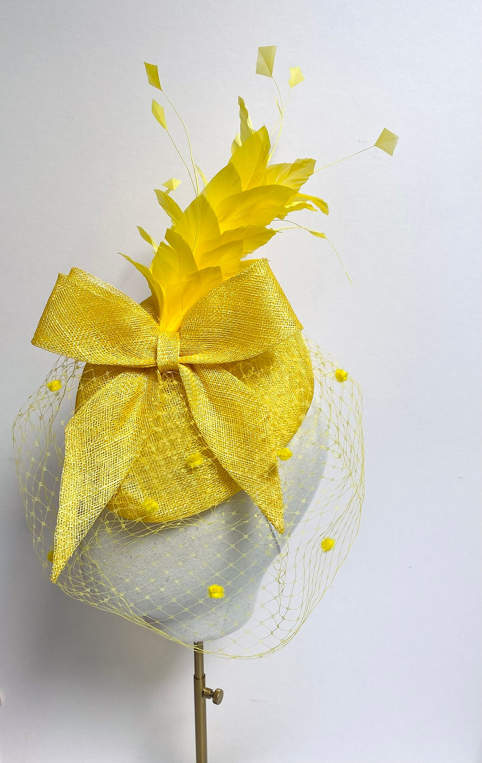 Thumbnail: A yellow feather fascinator with spot veiling and matching bow is displayed on a mannequin head
