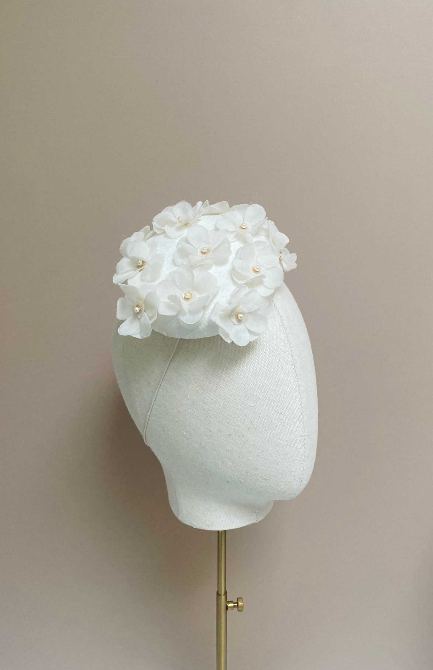 A small ivory wedding hat decorated with ivory flowers is displayed on a mannequin head