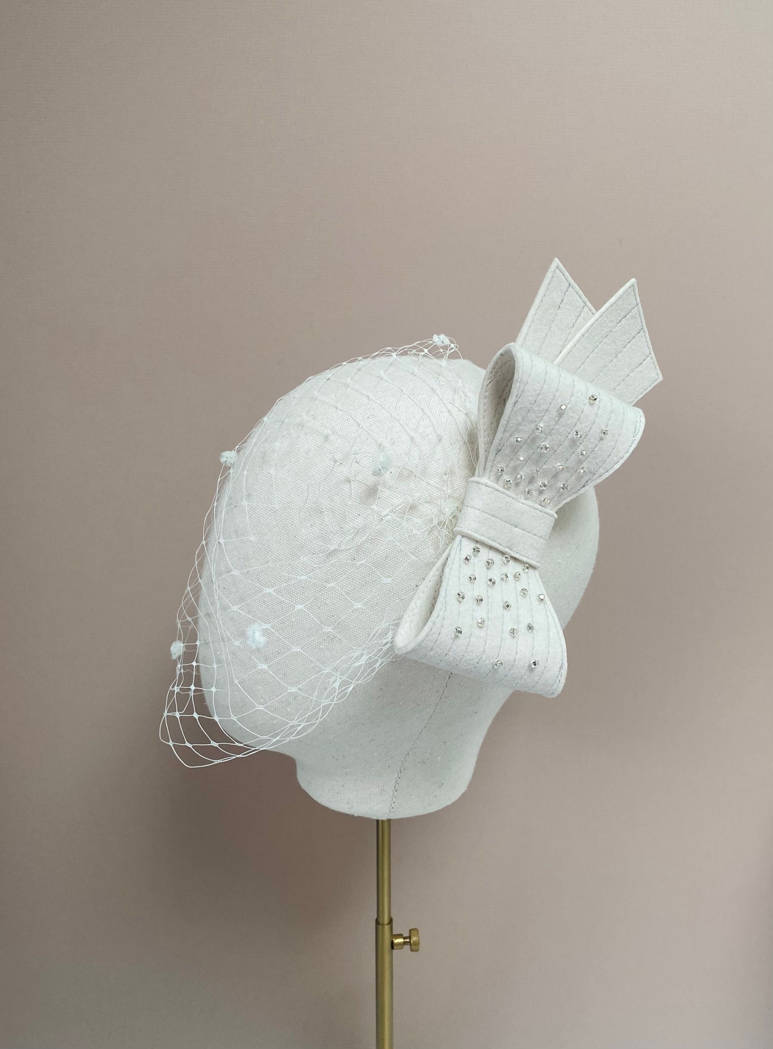 A birdcage wedding veil with an ivory felt beaded bow is displayed on a mannequin head