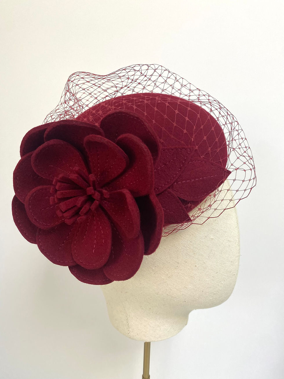 Thumbnail: A dark red felt flower wedding hat with a veil is displayed on a mannequin head