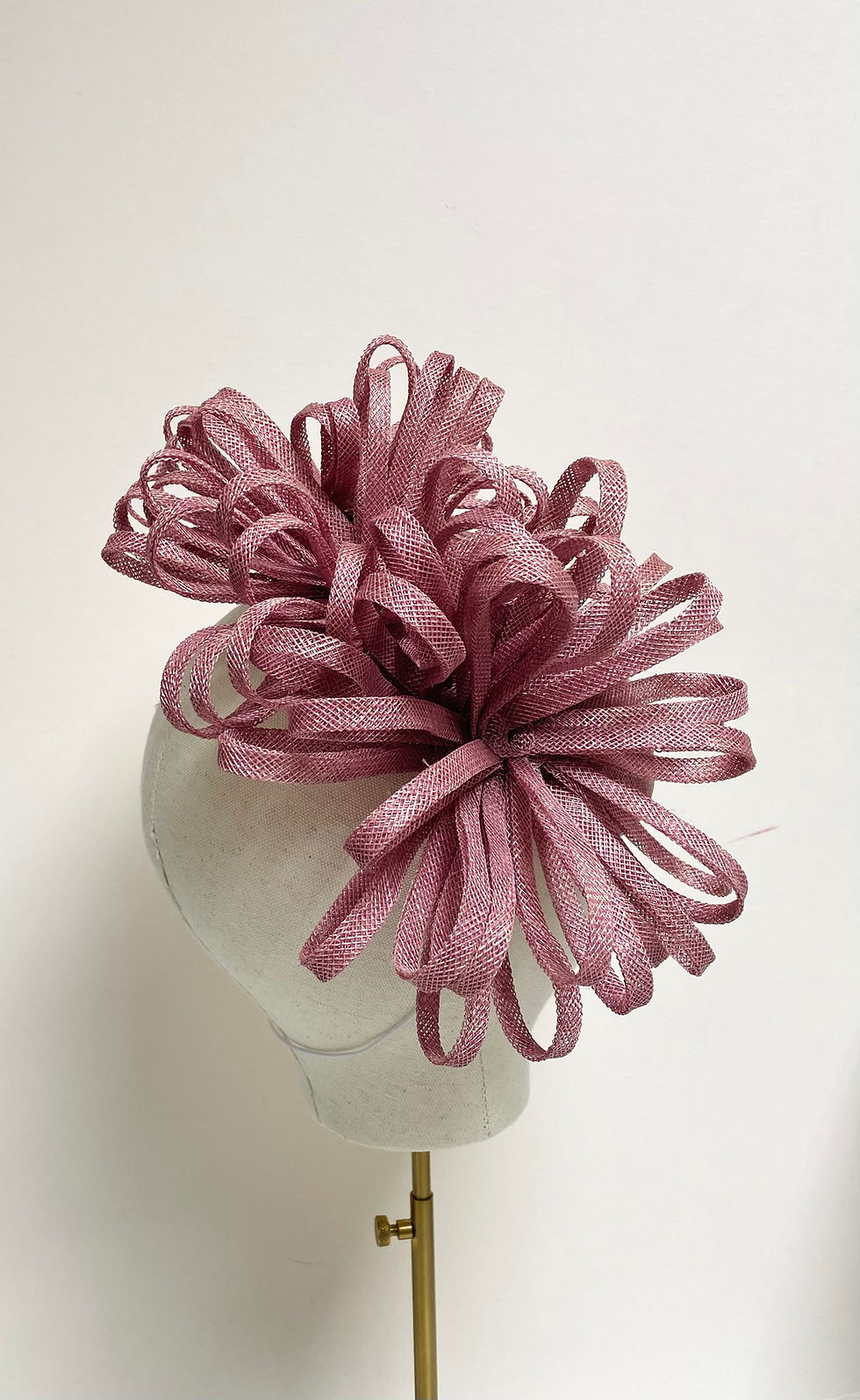 Thumbnail: A dusky pink sinamay hat decorated with matching loops is displayed on a mannequin head