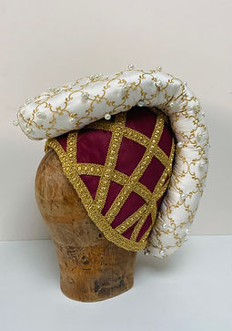 Side view of a red and gold medieval headdress decorated with gold braid and a gold and white padded roll.