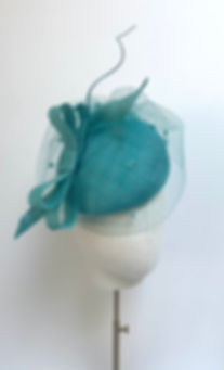 An aqua green wedding hat with a matching bow and spot veiling is displayed on a mannequin head