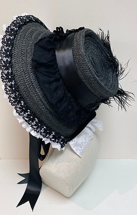 Side view of a black straw bonnet with white lace trim and a black feather is displayed on a mannequin head.