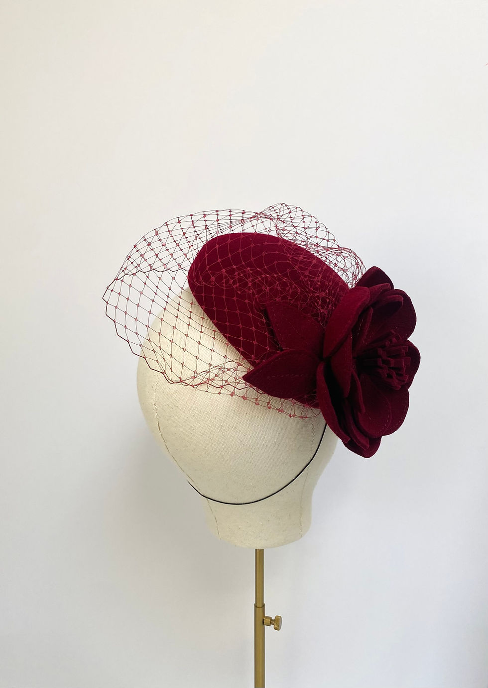 Thumbnail: A dark red felt flower wedding hat with a veil is displayed on a mannequin head