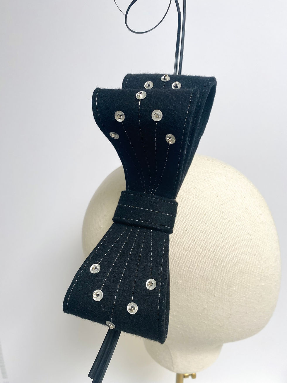Thumbnail: A large black felt bow headband decorated with ostrich quill feathers and silver sequins is displayed on a mannequin head