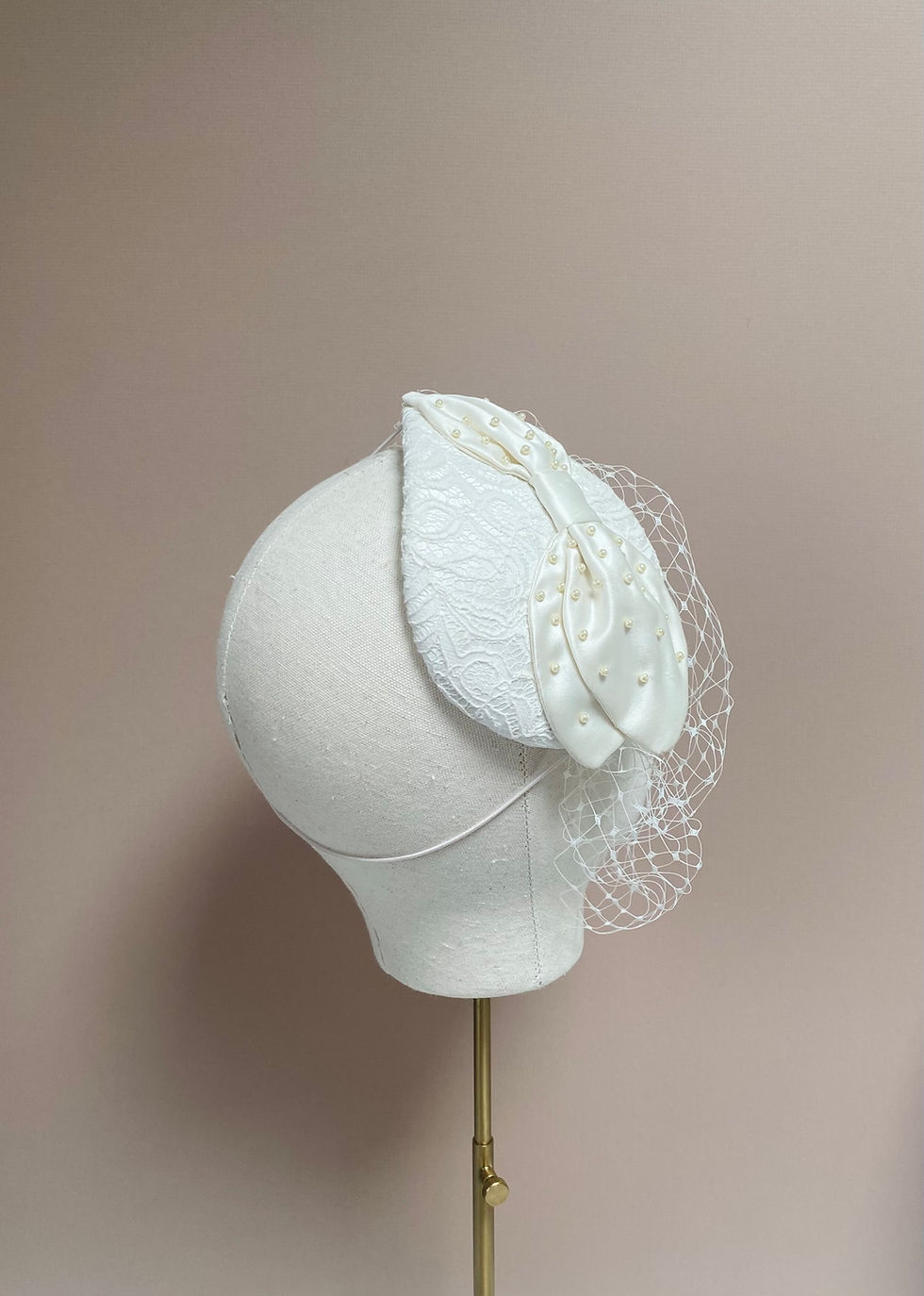 Thumbnail: An ivory lace wedding headpiece with a veil is displayed on a mannequin head