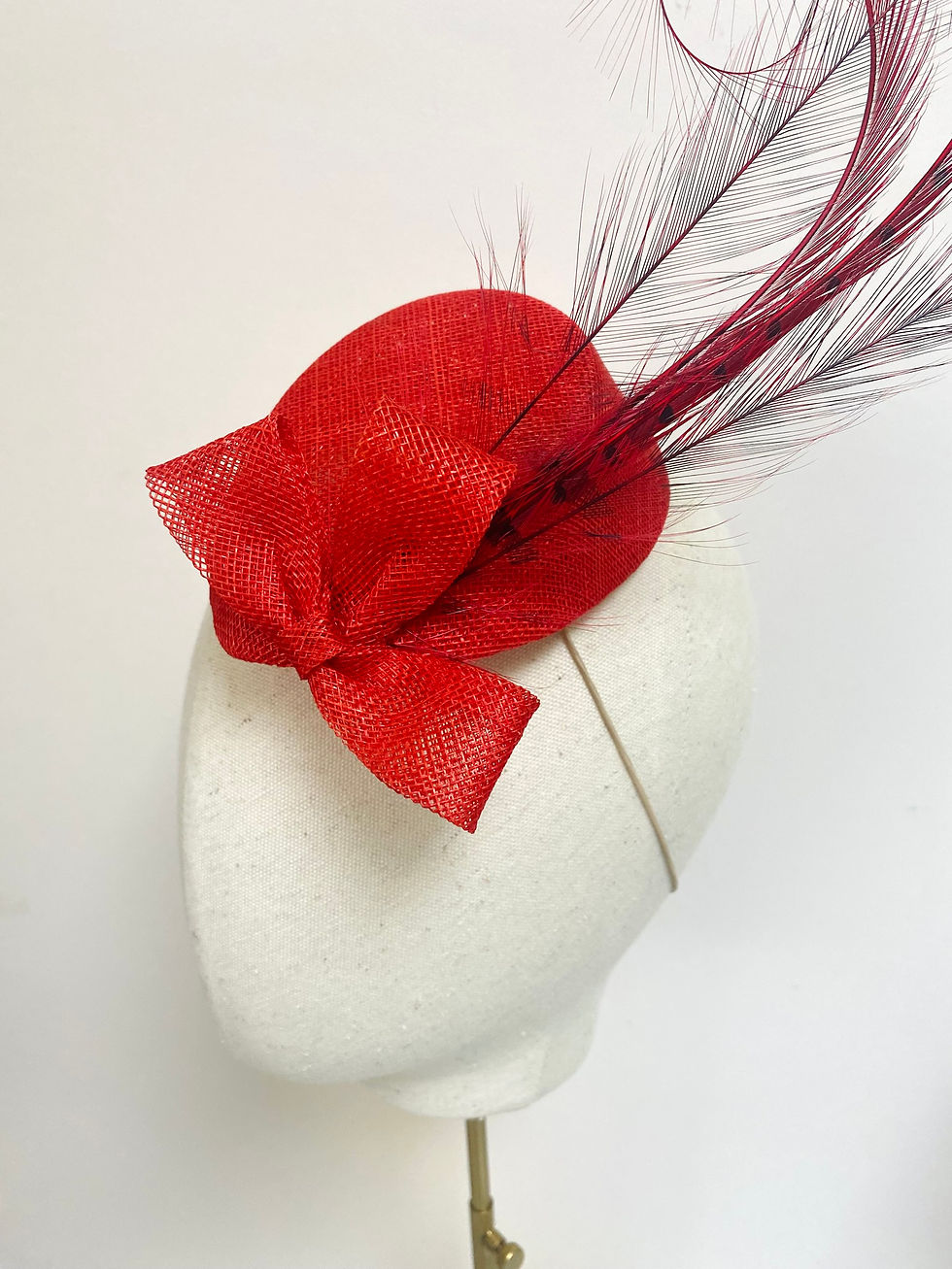Thumbnail: A red feather fascinator wedding guest hat is displayed on a mannequin head