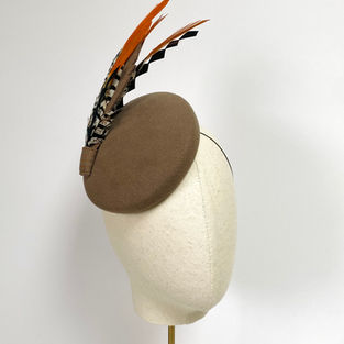 A mushroom felt round hat with feathers is displayed on a mannequin head with  a gold stand. 