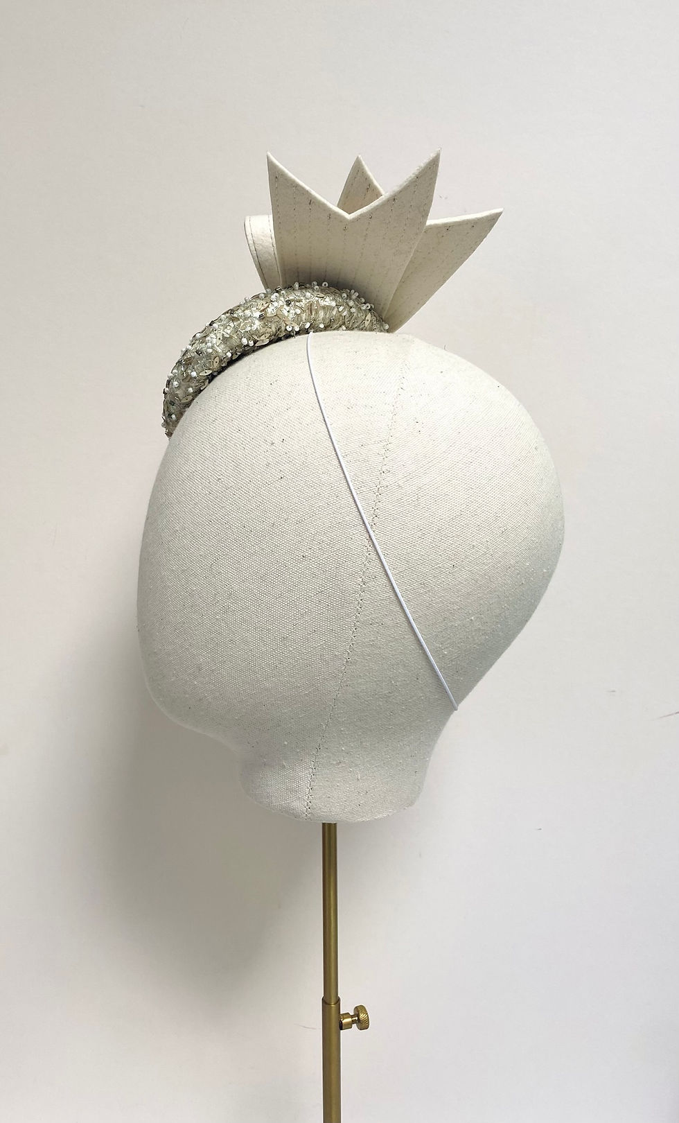 Thumbnail: A small round silver beaded wedding hat with a large ivory felt bow is displayed on a mannequin head