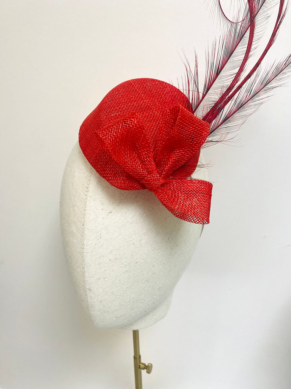 Thumbnail: A red feather fascinator wedding guest hat is displayed on a mannequin head