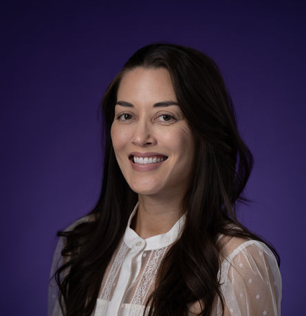Professional headshot of a smiling woman in a white blouse against a purple backdrop, photographed in Colorado for business use.