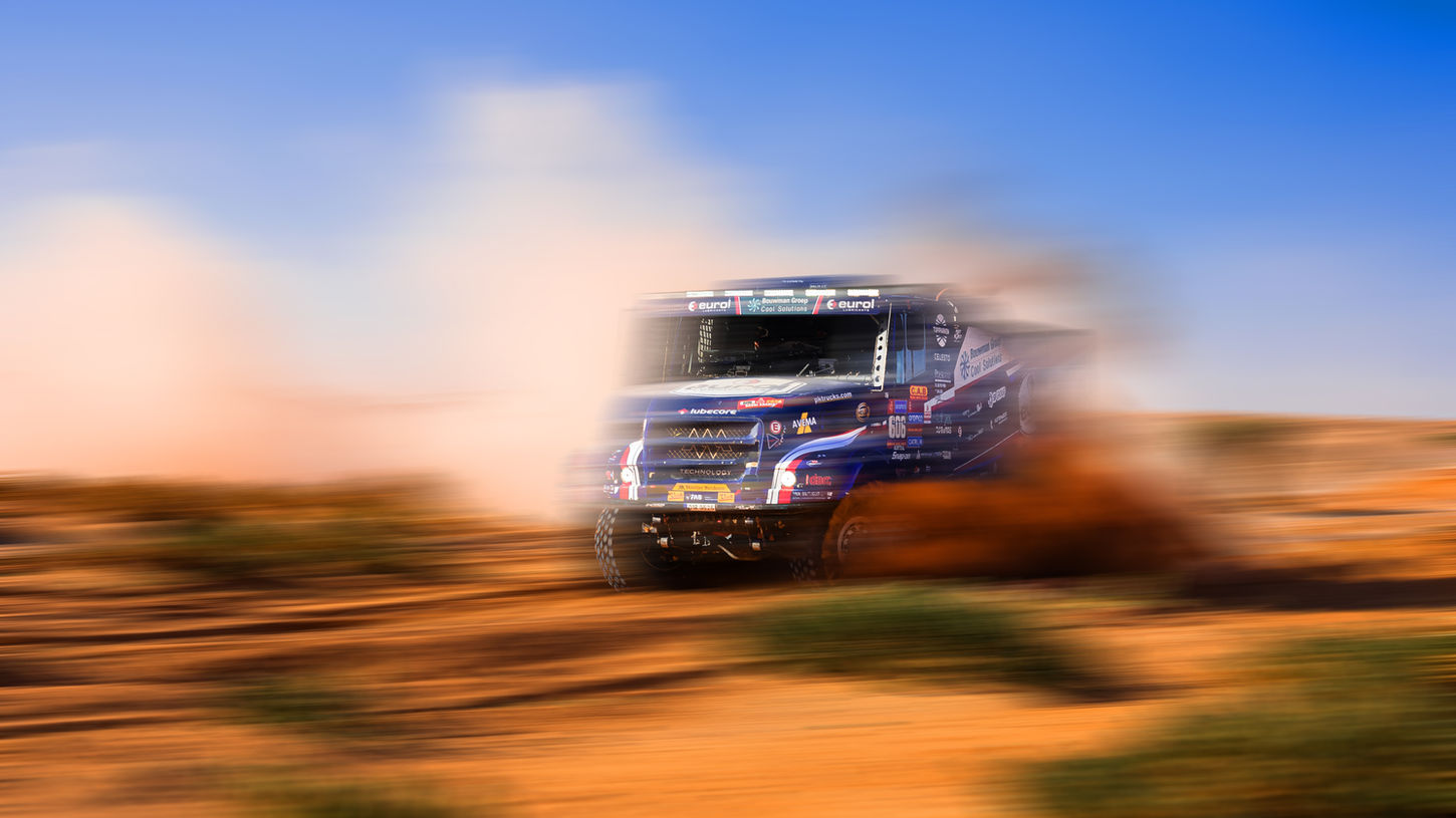 Off-road racing truck moving fast in a dusty, dry landscape.
