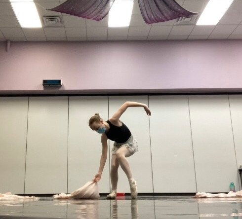 a ballet dancer gracefully picks up some fabric off of the floor.