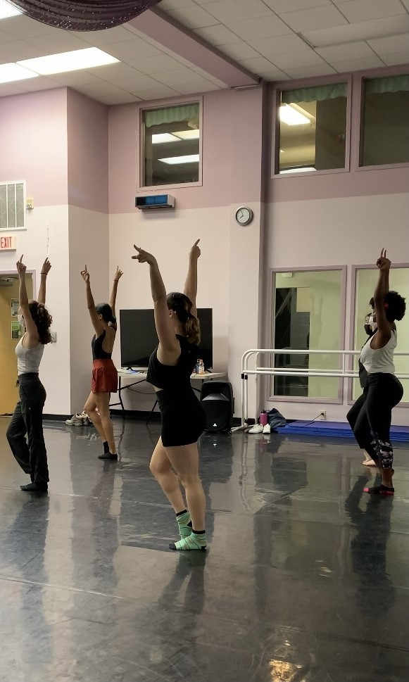 4 dancers with their hands in the air rehearse for a piece.