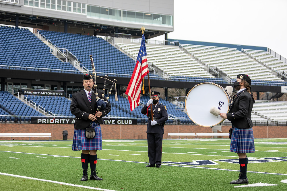 A piper, a drummer, and the american flag bearer on the football field.
