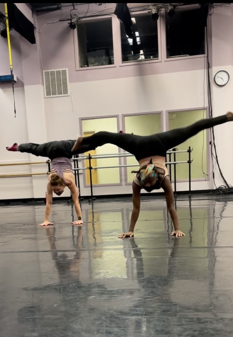 Two dancers in rehearsal doing a handstand with a full split.