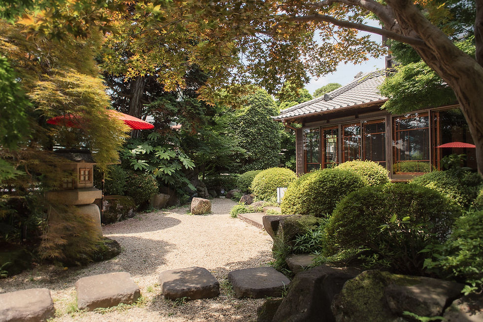 Japanese garden with lush greenery, stone path, red parasols, and a traditional wooden house, creating a serene, peaceful ambiance.