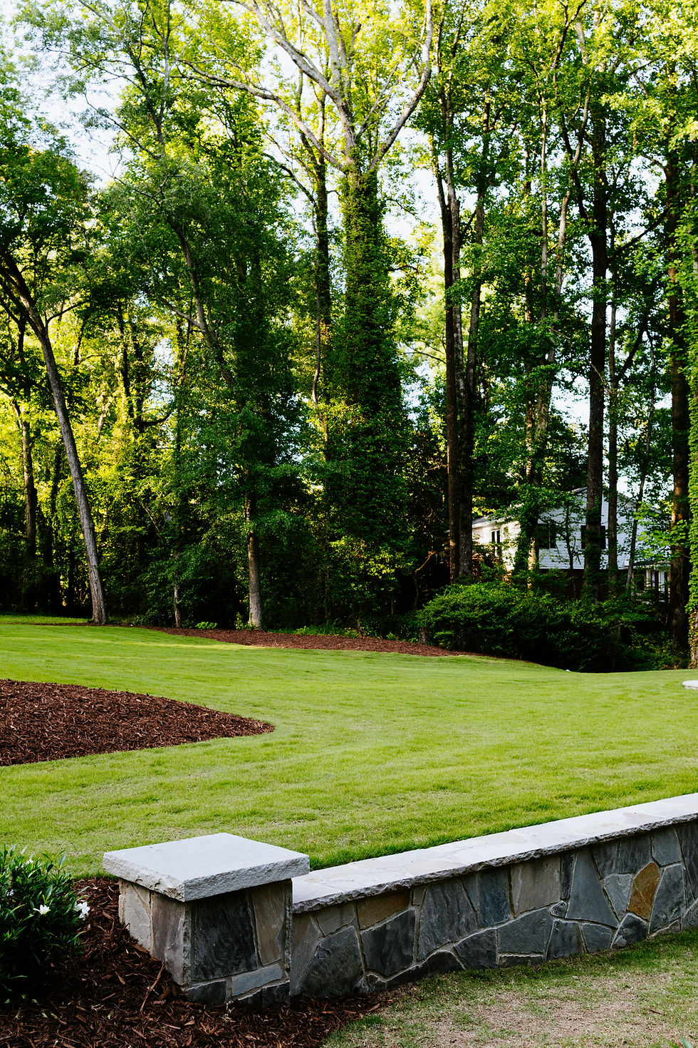 Green grassy lawn with plant bed and wooded background