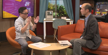 Two people in conversation on set, filming a bilingual or community-focused interview