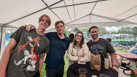 Four friends smile together casually posing under a white canopy at an event