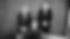 three attorneys, two standing one sitting on a couch in front of a wooden paneled wall